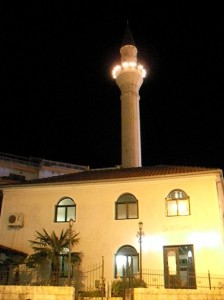 Xhamia e Kryepazarit Ulqin  Qyteti i Ulqinit, ndonëse i vogël, është mjaft i gjallë dhe i mbushur përherë me njerëz që shkojnë e vijnë në kërkim të diçkaje. Aty, ka përherë vizitorë që vijnë nga jashtë, shqiptarë të diasporës, që kthehen për të kaluar muajin e Ramazanit me të afërmit e dashamirët, me të cilët, jeta i ka ndarë cep më cep të botës...     Ramazani është edhe muaji i të ftuarve të ndryshëm të Bashkësisë Islame  të këtij qyteti, hoxhallarë, dijetarë, studiues, e personalitete të spikatura të Thirrjes Islame në trevat tona, që vijnë aty gjatë këtyre ditëve, për të pasuruar jetën islame në qytetin e vogël bregdetar. Dhe është kjo traditë e bukur dhe e domosdoshme për gjallërinë e Thirrjes Islame në një vend, që i jep vlera tradicionale dhe bashkëkohore kësaj Thirrje të lashtë në këtë qytet me vlera e traditë!     Sonte, në këtë natë të njëzetë, në mbyllje të dhjetëditëshit të dytë të këtij muaji, sëbashku me thirrësin islam Lavdrim Hamja, erdhëm për t’u falur në Ulqin.     Nga një vështrim i shpejtë në këto orë të para të kësaj nate të re, qyteti nuk ka ndonjë ndryshim të madh me ditët e netët e tjera jashtë Ramazanit, përveç ndonjë afisheje të varur në mur, tek-tuk, nëpërmjet së cilës urohen besimtarët me rastin e këtij muaji të begatë dhe urimeve të përzemërta që dëgjon nga e djathta dhe e majta, me rastin e këtij muaji.     Atmosfera e kësaj nate teravie në xhaminë e Kryepazarit, ku drejton teologu i nderuar, miku im, Rifat ef. Jusufi, është e këndshme dhe në harmoni me atmosferën e vetë muajit. Te dera e jashtme e saj, në krahun e djathtë, në pllakën e mermertë që qëndron si adresë e kësaj xhamie, shënohet: “Xhamia e Kryepazarit. E ndërtoi Nuradin begu, 1749”.     Nga brenda, xhamia e moçme, është e zbukuruar me shkrime të shumta kur’anore, lutje, fjala e Njësisë, deklamime të ndryshme islame etj, që duke i shtuar edhe llojet e kaligrafive arabe me të cilat janë kryer këto shkrime dhe ngjyrat e tyre, e bëjnë atë një xhami të veçantë e mjaft tërheqëse për këdo që e viziton dhe bëhet pjesë e xhematit të saj, qoftë edhe për një namaz.     Në ballinë të xhamisë, në të djathtë të mihrabit të zbukuruar me ajetet e kibles, me një shkrim naziq, lexohet ajeti kur’anor: “All-llahu nuk e prish gjendjen e një populli (nuk ua largon të mirat) përderisa ata ta ndryshojnë veten e tyre”[1]. Në krahun e djathtë të mihrabit, në njërin cep, është shkruar sureja “Keuther” e përballë saj, në formën e një varke shpëtimi, kushtet e besimit islam (amentu bil-lahi, ve melaiketihi, ve kutubihi, ve rusulihi, vel-jeumil-ahiri...).     Xhamia e Kryepazarit është e ndriçuar nga jashtë e nga brenda, sikurse është e pajisur me të gjitha pajisjet e nevojshme për kryerjen e ceremonive të ndryshme fetare. Në dalje të xhamisë, afër derës, qëndron një arkë e vogël, në adresë të së cilës shënohet: “Sadaka”. Është një gjetje interesante, që fton këdo për të kontribuar për xhaminë dhe nevojat e saj, duke ndjerë njëkohësisht edhe vlerën e sadekasë së dobishme.     Disa minuta para se të hynte koha e jacisë, me kërkesën dashamire të imamit të xhamisë, mbajta një vasë në lidhje me mirësinë e madhe që na është bërë si besimtarë, mundësia për të agjëruar muajin e madhërueshëm të Ramazanit, që njëkohësisht është edhe stinë e mëshirës, faljes dhe bamirësive të pakufi. Ndër të tjera fola edhe për madhështinë e mëshirës së All-llahut (xh.sh.) për krijesat e Tij dhe se si Ai e ka lënë të hapur derën e pendimit për ata që vrapojnë drejt saj, deri në momentet e fundit të jetës së tyre, duke iu referuar ajetit kur’anor: “Kush bën ndonjë të keqe ose e ngarkon veten, pastaj kërkon falje tek All-llahu, ai e gjen All-llahun Falës dhe Mëshirues”[2].     Namazin e jacisë dhe teravinë e drejtoi imami i ri Safet Resulbegu, një djalë i hajthëm, dashamirë në pamje të parë dhe komunikues. Me zërin e tij karakteristik, të fortë e të ëmbël, na dhuron kënaqësinë e përjetimit të çdo ajeti që lexon në njëzet rekatet e teravisë, pa përmendur jacinë me vitrin e saj.     Në përfundim të virdit, përqafimet e ngrohta hapin dyert e njohjeve të reja për mua, në xhaminë e Kryepazarit, në Ulqin. Imami i xhamisë, Rifat efendiu, më prezanton me imamin e Qendrës Islame Shqiptare Amerikane, në Kuins të Nju Jorkut (ShBA), z. Jusuf Bolaj, i cili ka ardhur nga shumë larg për të kaluar Ramazanin e këtij viti me të afërmit e miqtë e tij në Ulqin.     Pas prezantimit të parë, biseda jonë sillet rreth aktiviteteve të Qendrës Islame atje, themelimit të saj, kontributit për tubimin e shqiptarëve atje dhe të tjera çështje që lidhen me përparimin e Thirrjes Islame në qendrat tona të banimit e të veprimtarisë thirrëse.     Nata e njëzetë e këtij Ramazani në Ulqin, ishte si një frymëmarrje e re për ne, edhe për faktin e takimit me disa prej hoxhallarëve të nderuar të këtij qytetit, njohjen me imamin shqiptar me aktivitet në Nju Jork, vasin para xhematit ulqinak, këmbimin e eksperiencave personale në shërbim të Thirrjes Islame etj.     Kthimi për në Shkodër, ndonëse në një orë të vonë, shoqërohet nga qetësia e mesnatës, drita e hënës që rrezaton ëmbël mbi ne, freskia e vjeshtës e zëri i ëmbël i Gamidiut, që me ajetet e Librit, i shton kësaj nate të begatë përshpirtësi dhe prehje...     Në orët e para të një dite të re që është nisur drejt nesh, Shkodra është thuajse e përgjumur. Sheshi para xhamisë së Parrucës prehet në paqe. Me siguri, edhe ai ka kaluar një ditë të lodhshme (iftarin e madh të shtruar në mes të sheshit, nga minibashkia “Bajram Pasha” e Stambollit), por të këndshme, sikurse edhe ne, përtej kufirit... Autor / Thirrësi islam Muhamed Sytari